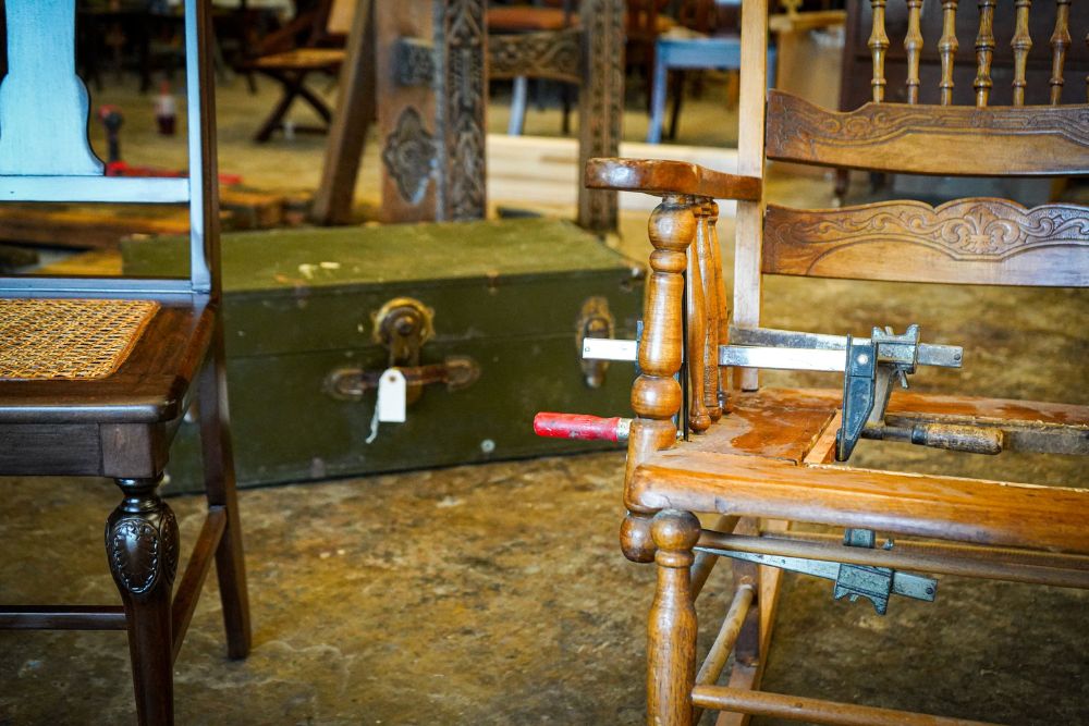 A wooden chair being repaired with clamps next to a table, with a green suitcase on the floor.