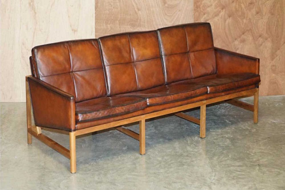 Vintage leather brown sofa with three cushions and a wooden frame, representing classic Danish design aesthetics.