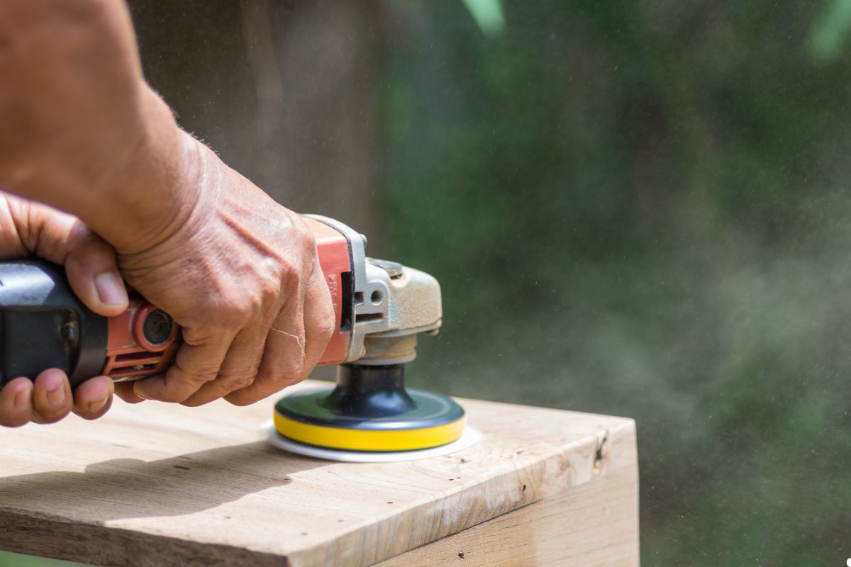 A person operates an electric sander on a wooden table, smoothing the surface for a polished finish.